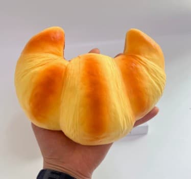 Golden croissant-shaped PU squishy with layered bakery texture held in a hand