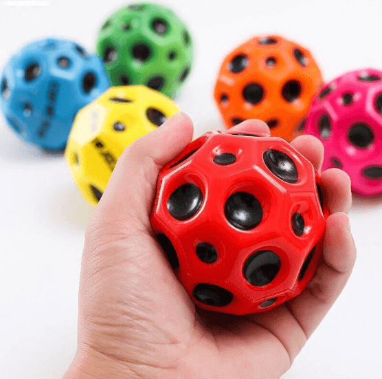 Red PU high rebound ball held in a hand with blue green yellow orange and pink balls in the background
